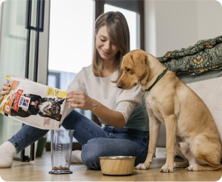Eine Frau füllt Hill's Pet Nutrition Futter in einen Messbecher, während ein Hund aufmerksam zusieht.