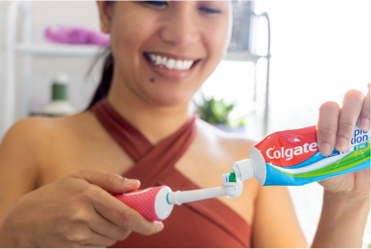 Eine lächelnde Frau, die im Badezimmer Colgate-Zahnpasta auf eine Zahnbürste gibt.